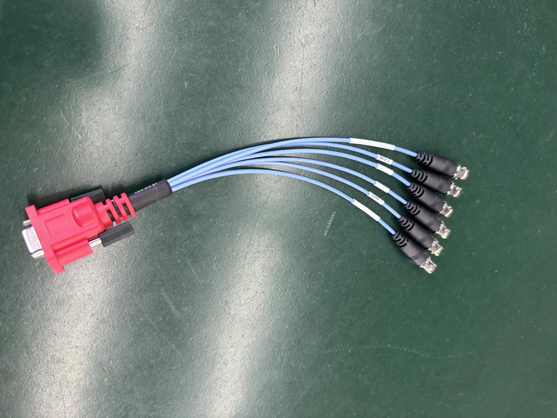 Red D-sub breakout cable assembly photographed on a green factory floor